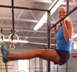 Girl hanging on the horizontal bar with raised legs.