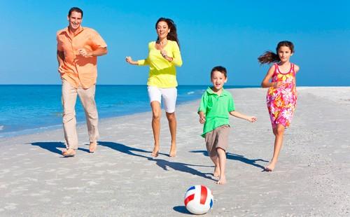 Parents avec enfants botter un ballon sur la plage.