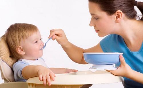 Young mother feeds her son from a spoon