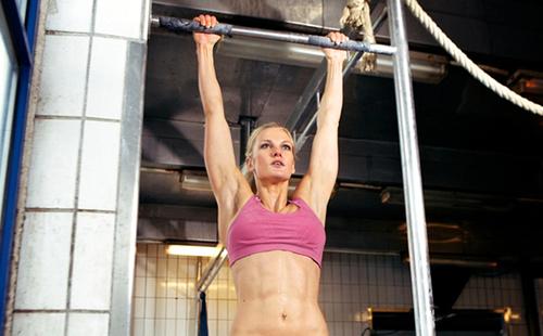 Blonde in pink minitope pulls herself up on a horizontal bar