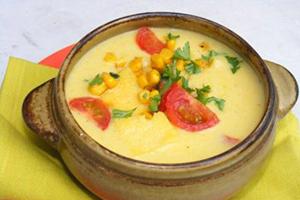 Yellow corn, greens and tomatoes in a clay pot