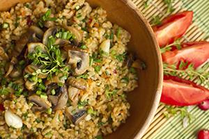 Bulgur with mushrooms and herbs in a wooden bowl and tomato slices