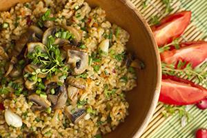 Bulgur aux champignons et aux herbes dans un bol en bois et des tranches de tomates