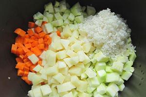 Zucchini and carrots chopped into cubes and a handful of rice in a multicooker bowl