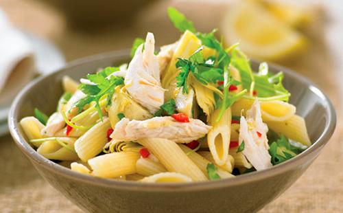 Large pasta with pieces of chicken and herbs in a ceramic bowl