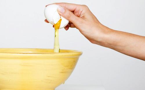 Hand breaks an egg in a wooden bowl