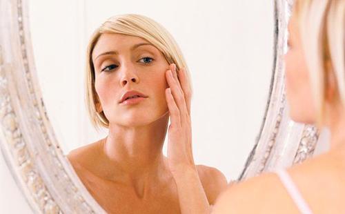 La rubia examina cuidadosamente la piel en las esquinas de los ojos en un espejo.