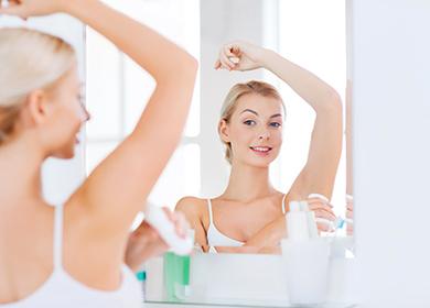 Woman with deodorant in front of a bathroom mirror