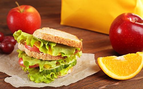 Sandwich con ensalada verde, rodaja de naranja y manzanas rojas para el desayuno