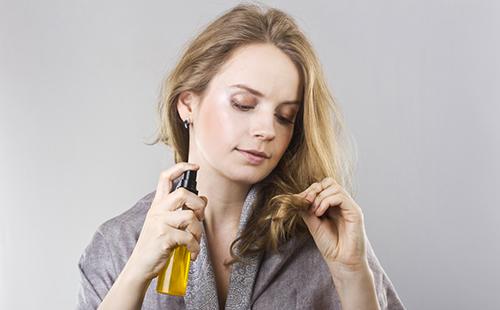Fille avec une bouteille d'huile examine les extrémités des cheveux