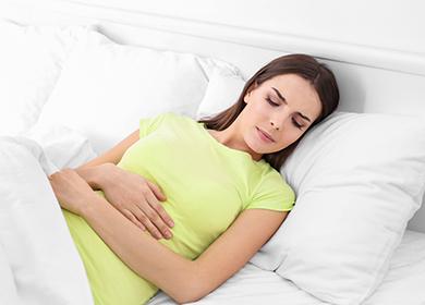 Joven mujer yace en la cama abrazando su vientre