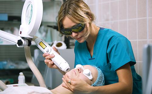 Esteticista trata la cara del paciente con un láser.