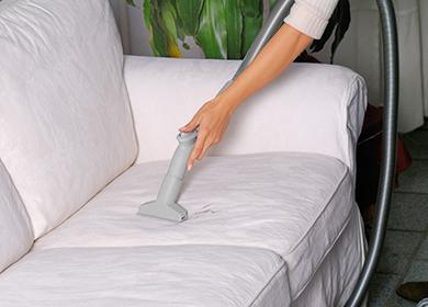 Woman cleans a light sofa with a vacuum cleaner