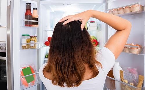 Une femme perplexe jette un coup d'œil dans le frigo
