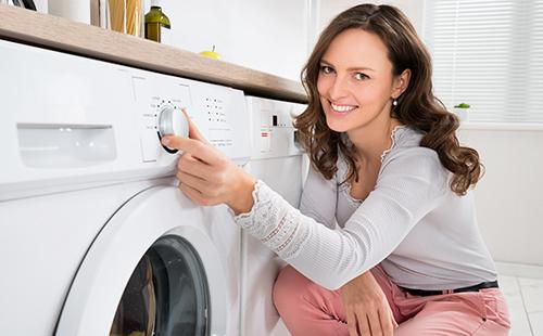 Woman with a smile turns on the washing machine