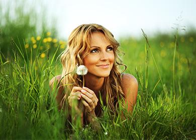 Beautiful blonde lies on the grass and holds a dandelion in her hands