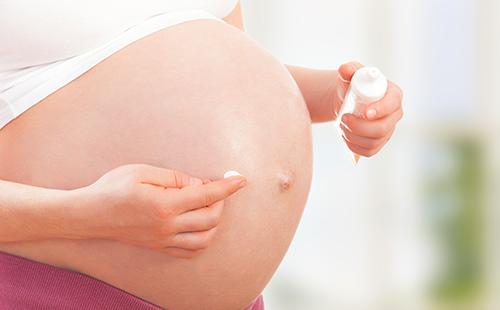 Mujer embarazada aplica crema en el vientre