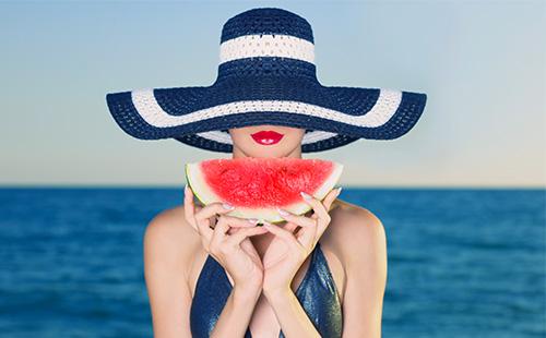 The girl in the hat holds a slice of watermelon
