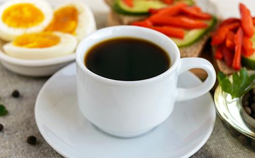 Una taza de café fuerte, huevos duros y verduras para el desayuno.