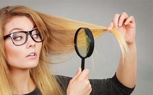 Blonde examines her hair in a magnifying glass