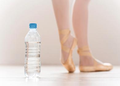 Botella de agua y bailarina bailando piernas en el fondo