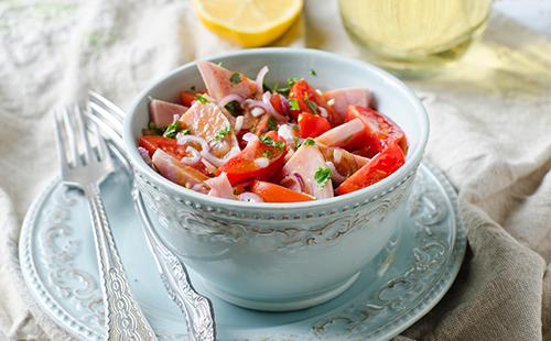 A cup of salad with ham and tomatoes