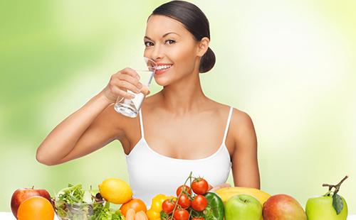 Mujer en un top blanco con un vaso de agua y fruta.