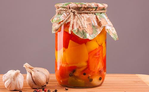 On the table is a jar with canned vegetables, garlic and spices.