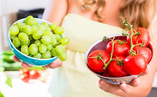 Mujer sostiene tomates y uvas en tazas