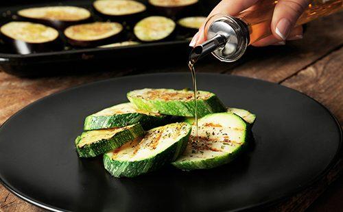 Female hand pours oil on slices of zucchini