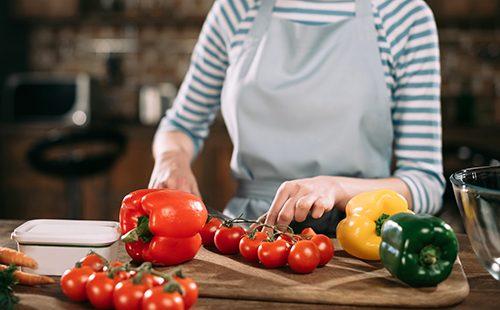 Mujer corta tomates y pimientos en una ensalada