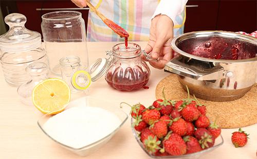 Woman pours strawberry jam into jars