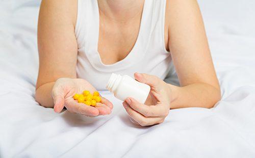 Woman in bed holds yellow pills