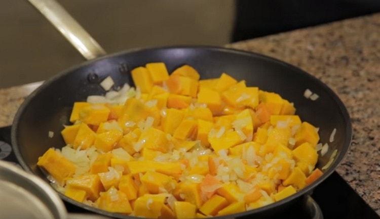 Cebollas, zanahorias y trozos de calabaza se pasan en una sartén.