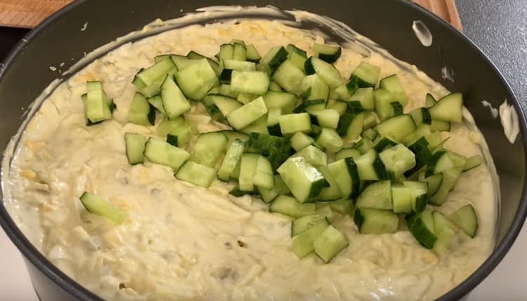 Dice a fresh cucumber and form the next layer of salad from it.