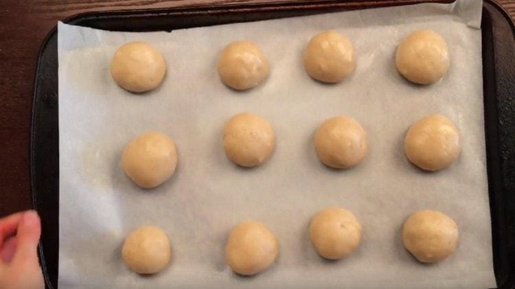 Avec les mains mouillées, nous roulons les boules de la pâte et les posons sur une plaque à pâtisserie recouverte de papier sulfurisé.