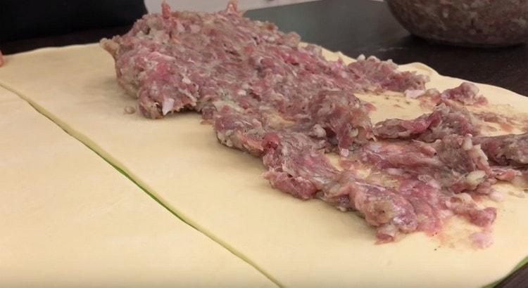 Pour chaque moitié de la pâte, nous étalons la viande hachée avec une couche uniforme, en nous retirant d'un bord sur quelques centimètres.