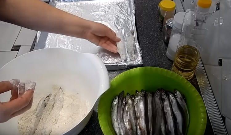 Enrolle cada pescado en harina y extiéndalo en filas en una bandeja para hornear.