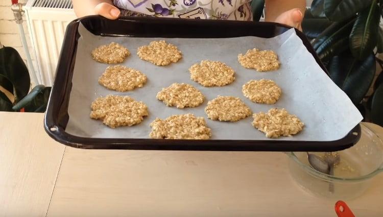 Nous répandons la farine d'avoine avec une cuillère et la nivelons avec une cuillère pour former des biscuits ronds.