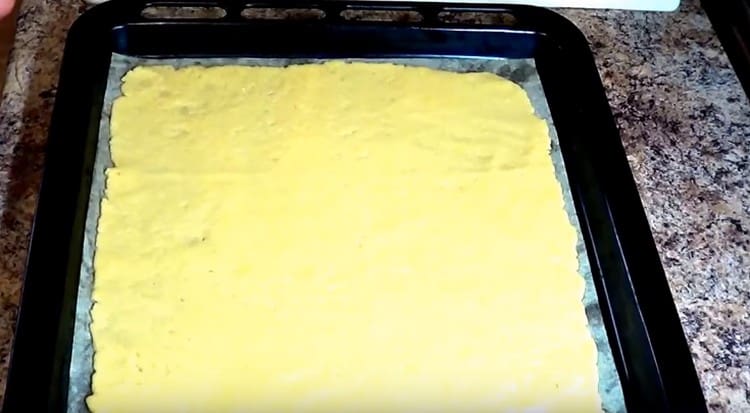We cover the baking sheet with parchment and stretch a larger piece of dough on it.