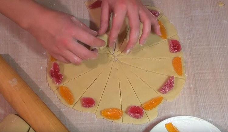 À la base de chaque triangle de pâte, mettez un morceau de marmelade et enroulez-le avec un rouleau, formant un bagel.