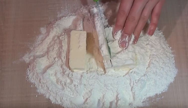 Nous répandons le beurre froid dans la farine et le hachons en petits morceaux avec un couteau.