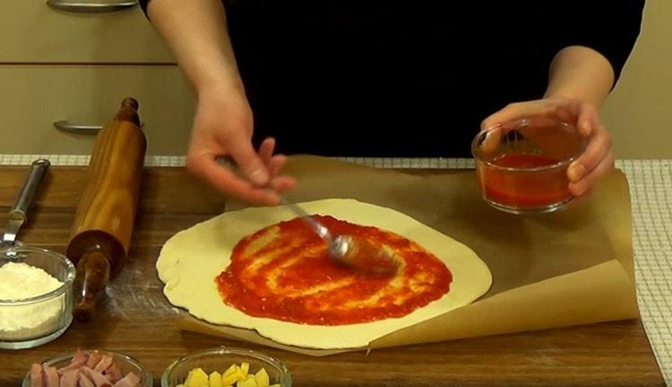 Graisser la pâte avec de la sauce tomate.