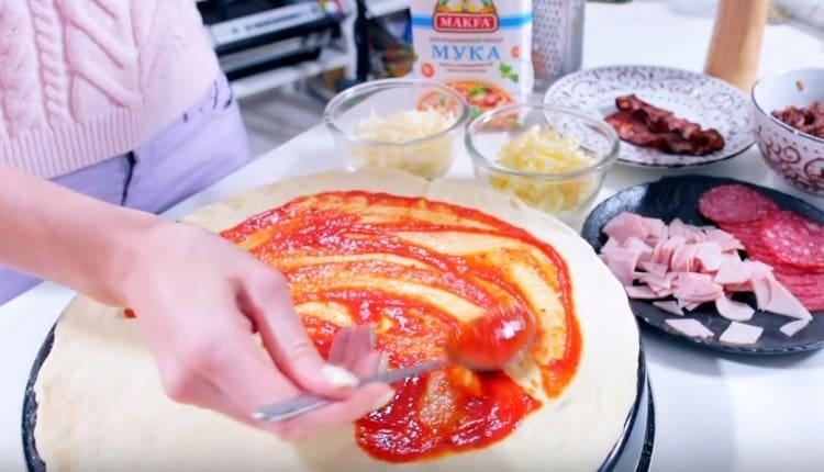 Graisser la pâte avec de la sauce tomate.