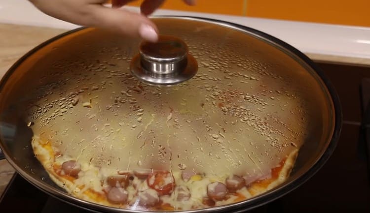Nous mettons la casserole avec pizza sur le feu, couvrons avec un couvercle.