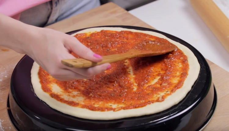 Luego, engrase la base para pizza con salsa de tomate.