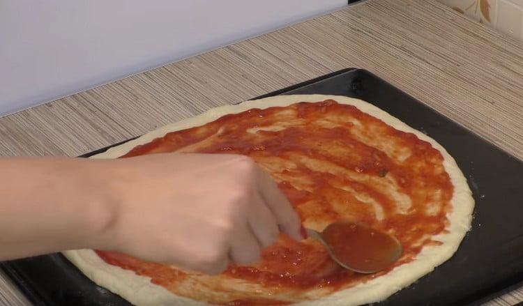 Lubricate the base for pizza with tomato sauce.