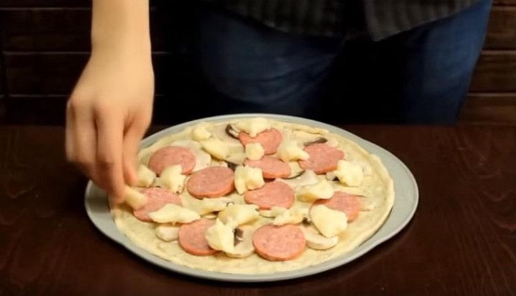 Podlogu za pizzu podmažite bijelim umakom, širite nadjev.