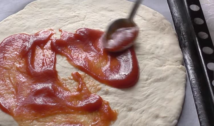 Graisser la base pour la pizza à la sauce tomate.