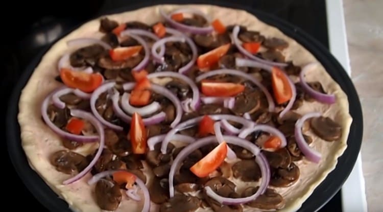 Nous répandons les champignons, les olives, les tomates, les oignons sur la base de la pizza, saupoudrons d’ail.